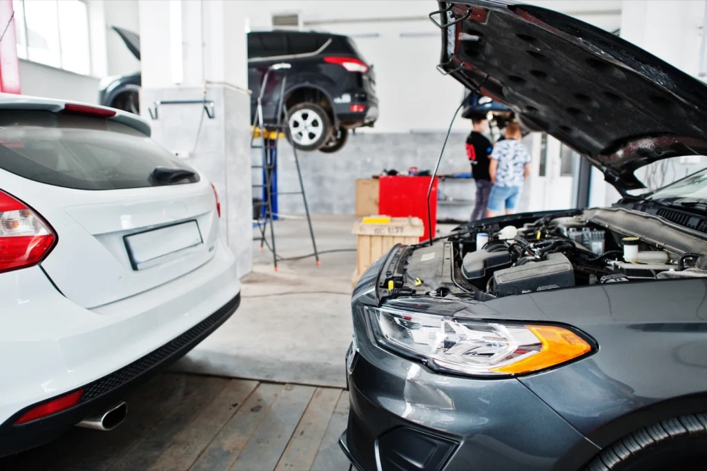Car workshop with an open bonnet in the foreground and a car on a lift in the background